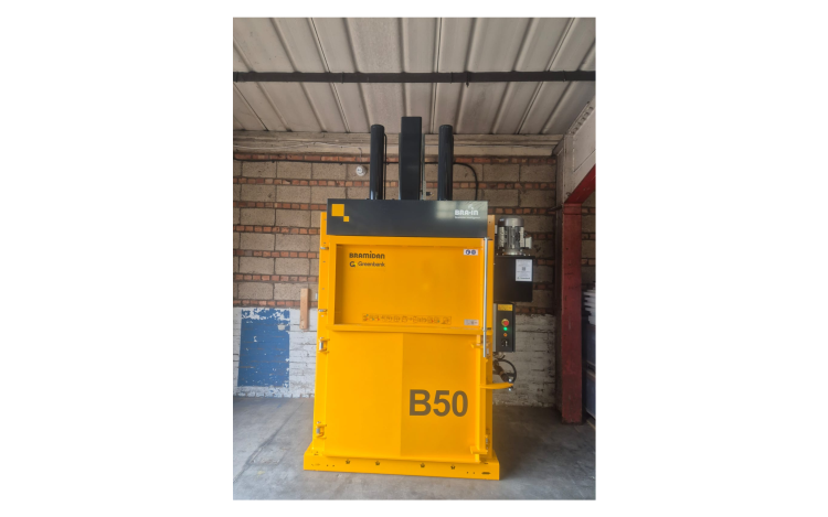 yellow vertical baler against brick wall.